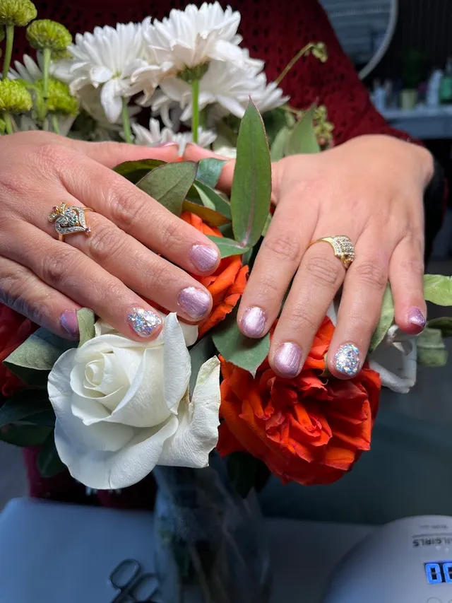 Nail art held against white and orange roses